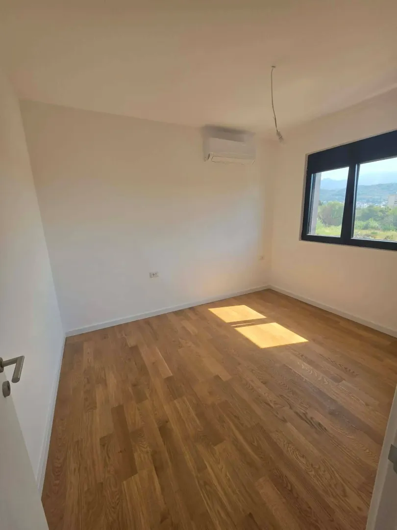 Empty room with wooden flooring, an air conditioning unit, and a window.