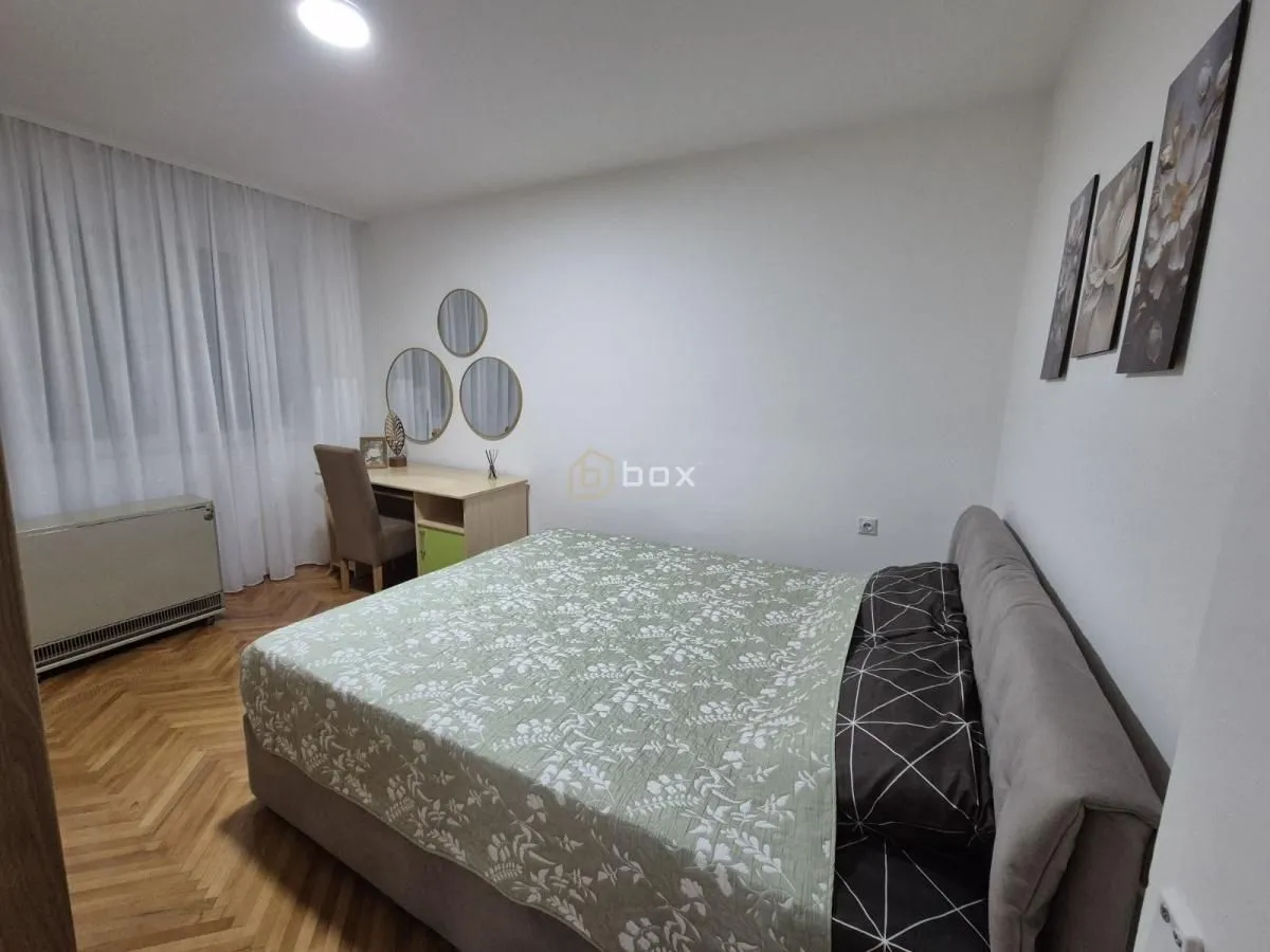 Nameštena spavaća soba sa bračnim krevetom, radnim stolom i ukrasnim ogledalima na zidu.