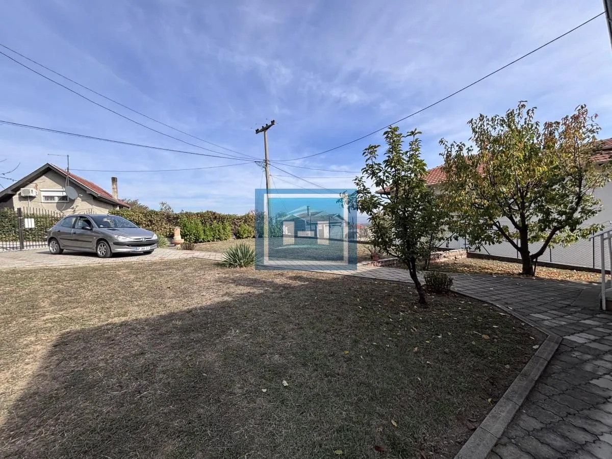 Dvorište sa travnjakom, drvećem i parkiranim automobilom ispred kuće.
