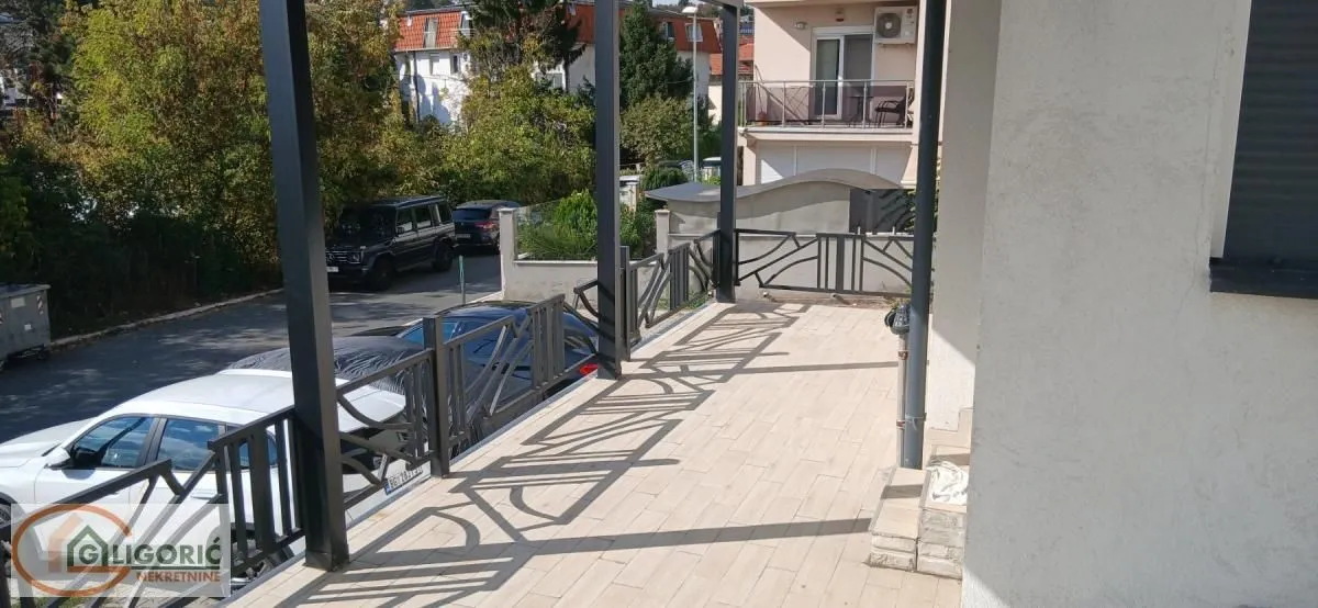 Prostrana natkrivena terasa sa metalnom ogradom i pogledom na ulicu i parking.