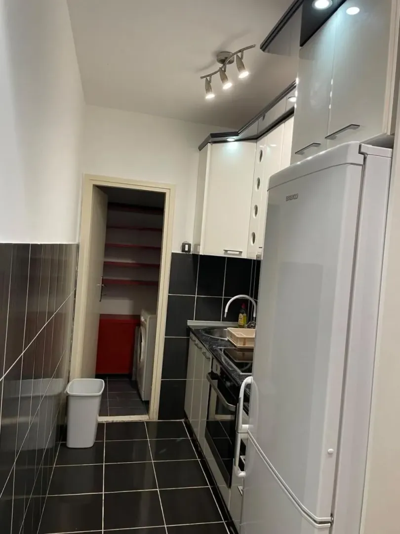 Small kitchen with white cabinets and a refrigerator, with a view of the pantry.