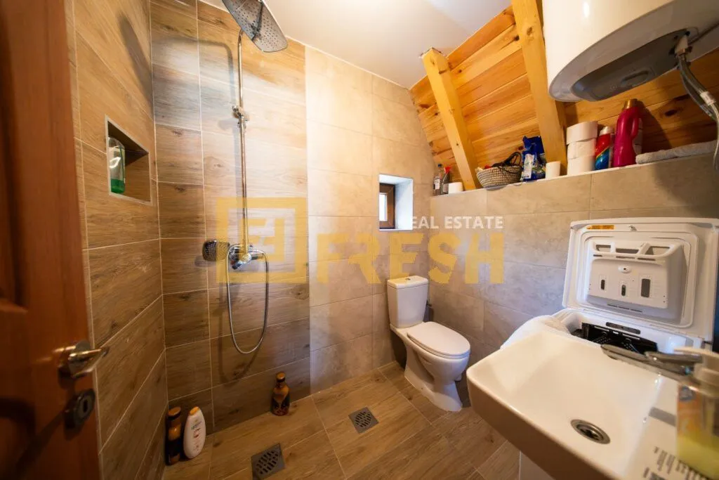 Kupatilo sa tuš kabinom, WC šoljom, umivaonikom i veš mašinom u potkrovlju.
