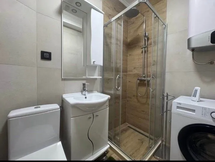 Compact bathroom with a shower cabin, sink, toilet, and washing machine.
