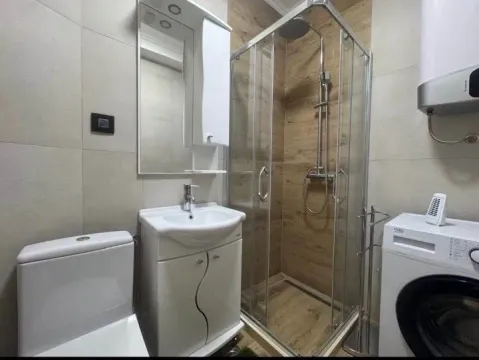 Compact bathroom with a shower cabin, sink, toilet, and washing machine. - image 4