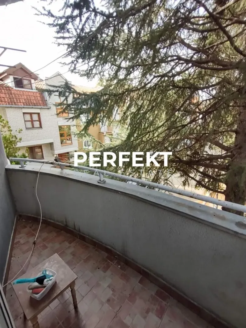 Manji popločani balkon sa pogledom na susedne zgrade i drveće.