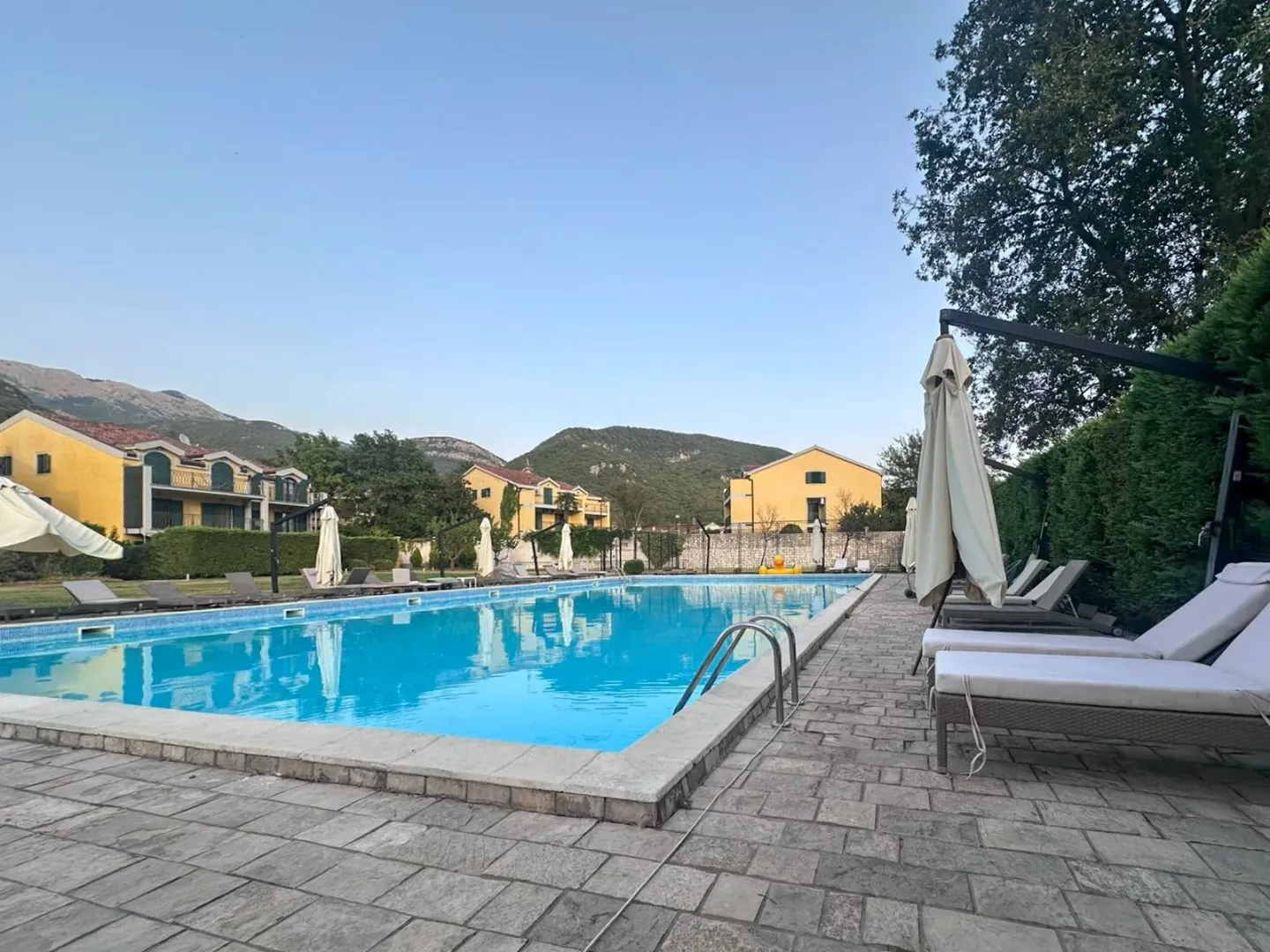 Veliki vanjski bazen sa ležaljkama i suncobranima okružen zgradama i planinama.