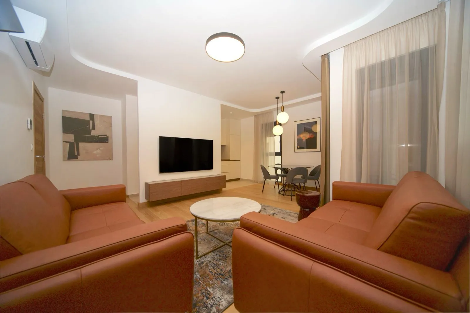 Living room with leather sofas, television, and a dining area in the background.