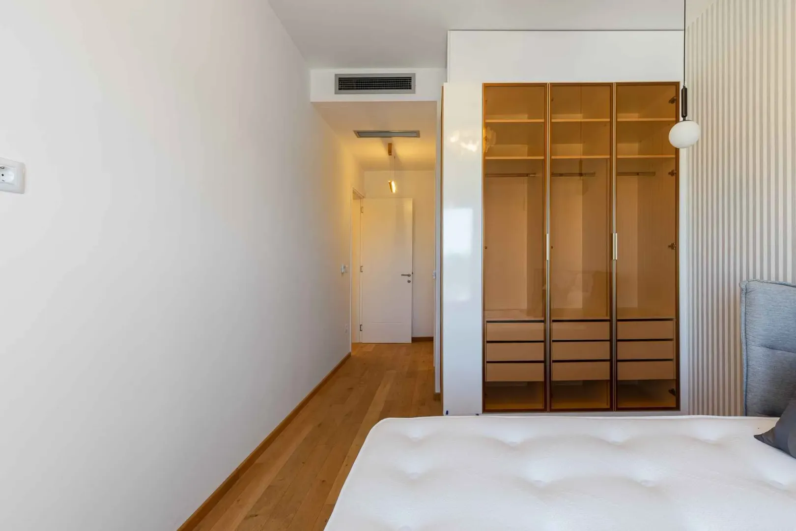Svijetla spavaća soba sa modernim ugradnim garderoberom sa staklenim vratima.