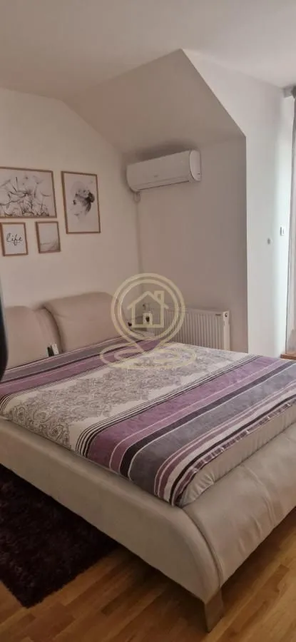 Nameštena spavaća soba sa bračnim krevetom, klima uređajem i zidnim slikama.
