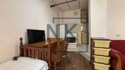 Small living room with a desk and a kitchen in the background. - image 5