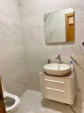 Modern bathroom with a sink, mirror, and toilet tiled with marble-patterned tiles. - image 10