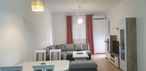 Svijetla dnevna soba sa sivom ugaonom garniturom, trpezarijskim stolom i TV regalom. - image 3