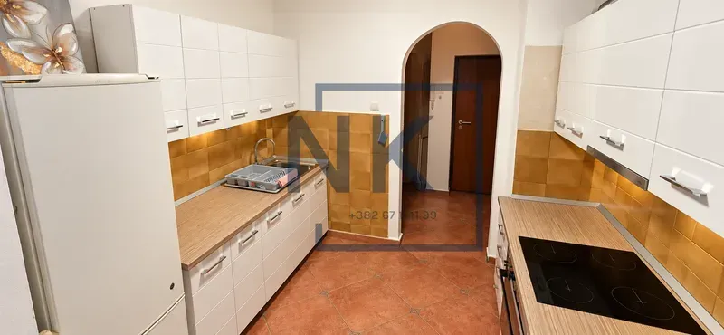 Kuhinja opremljena bijelim elementima, frižiderom i ugrađenom pločom za kuvanje.