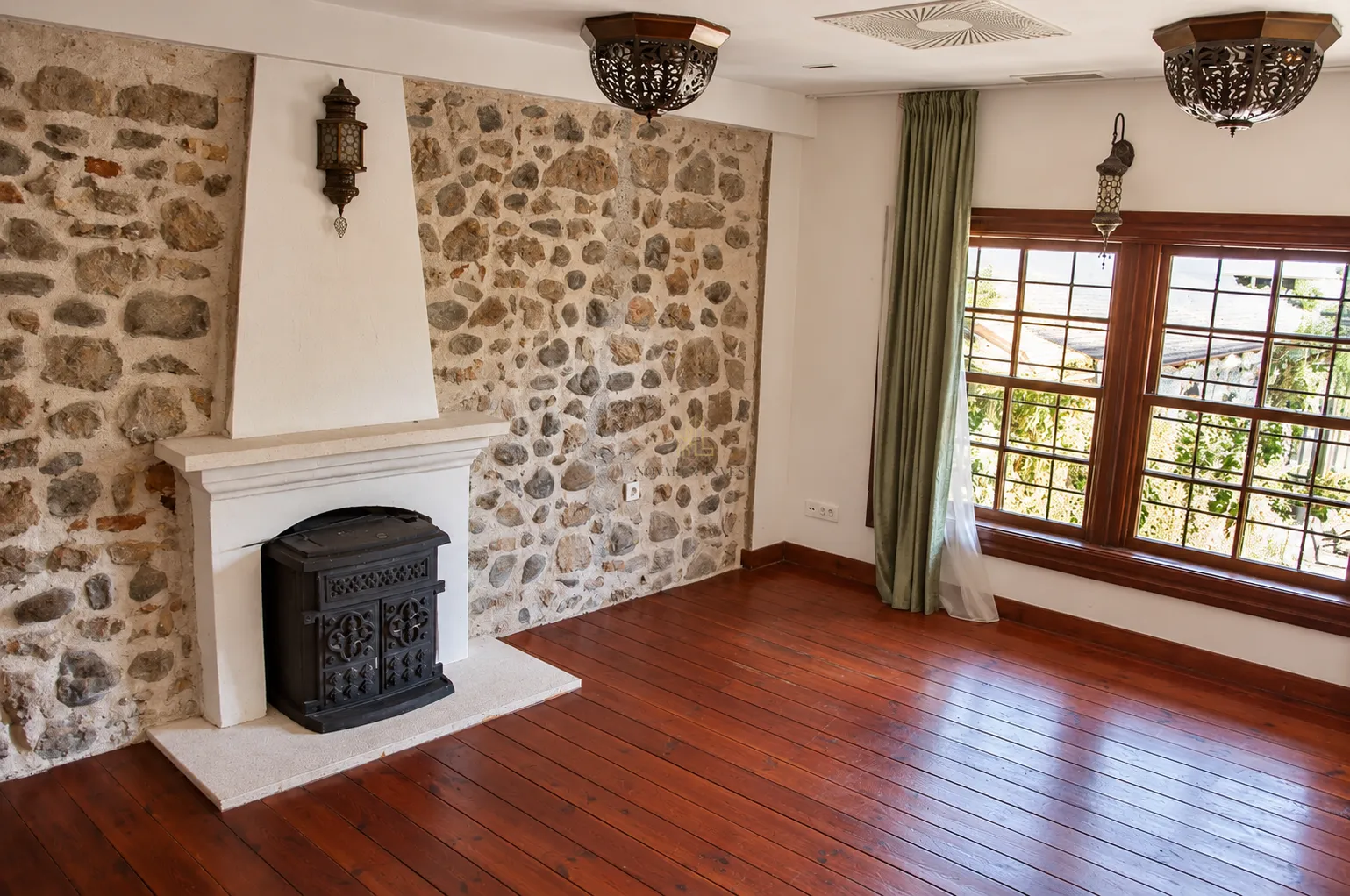 Living room featuring a fireplace, a stone wall, wooden flooring, and a large window.
