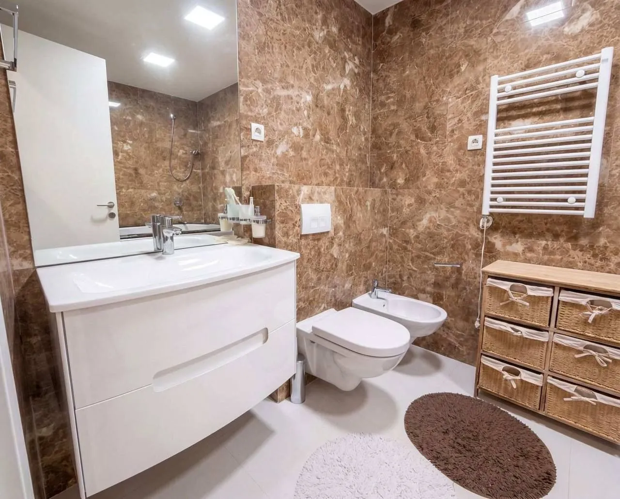 Modern bathroom equipped with a vanity, toilet, bidet, and marble tiles.