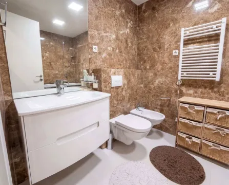 Modern bathroom equipped with a vanity, toilet, bidet, and marble tiles. - image 15