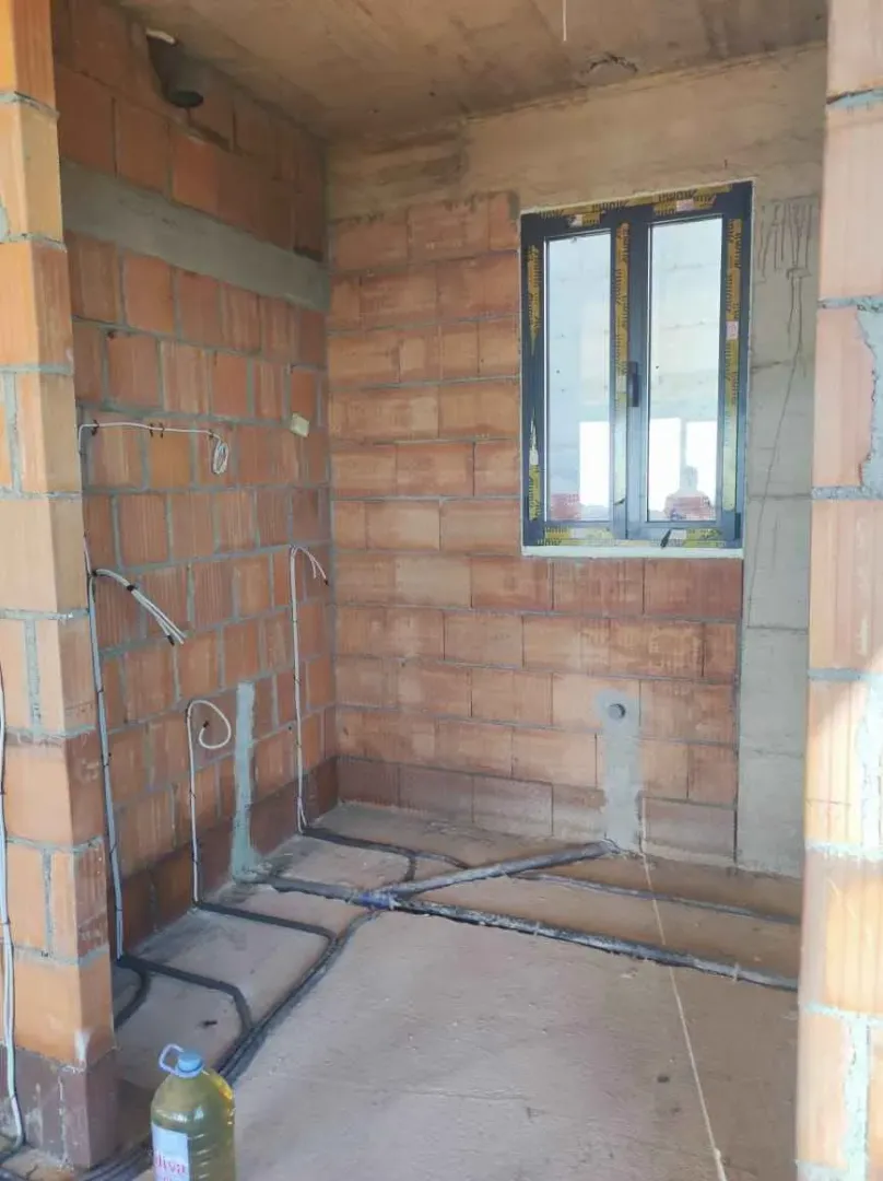 Nepreuređena prostorija u izgradnji sa instalacijama i prozorom.