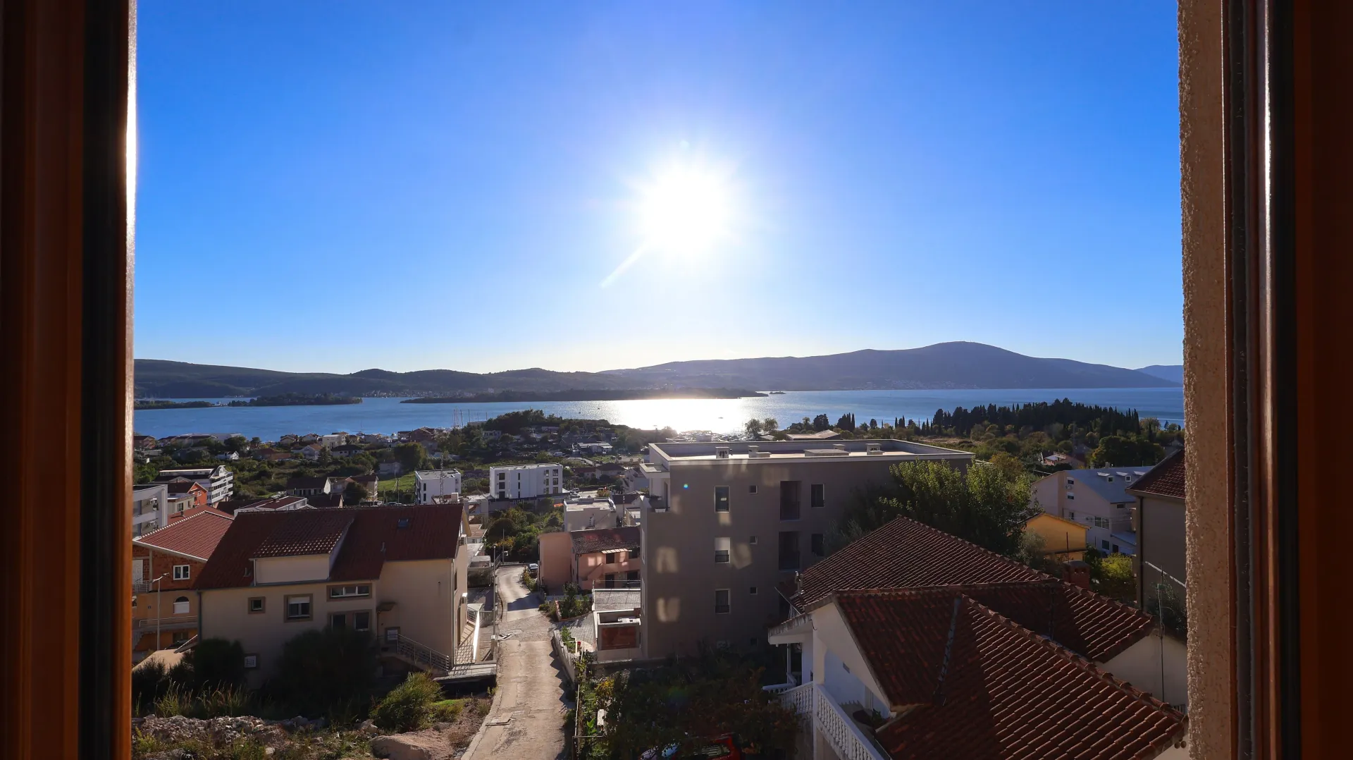 Pogled sa prozora na okolno naselje i zaliv sa brdima u pozadini.