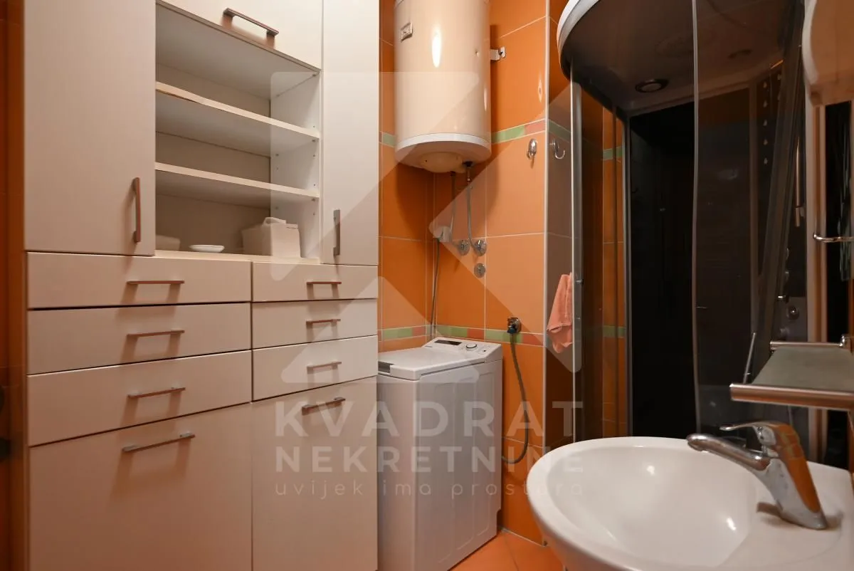 Bathroom with a shower cabin, washbasin, cabinet, and washing machine.