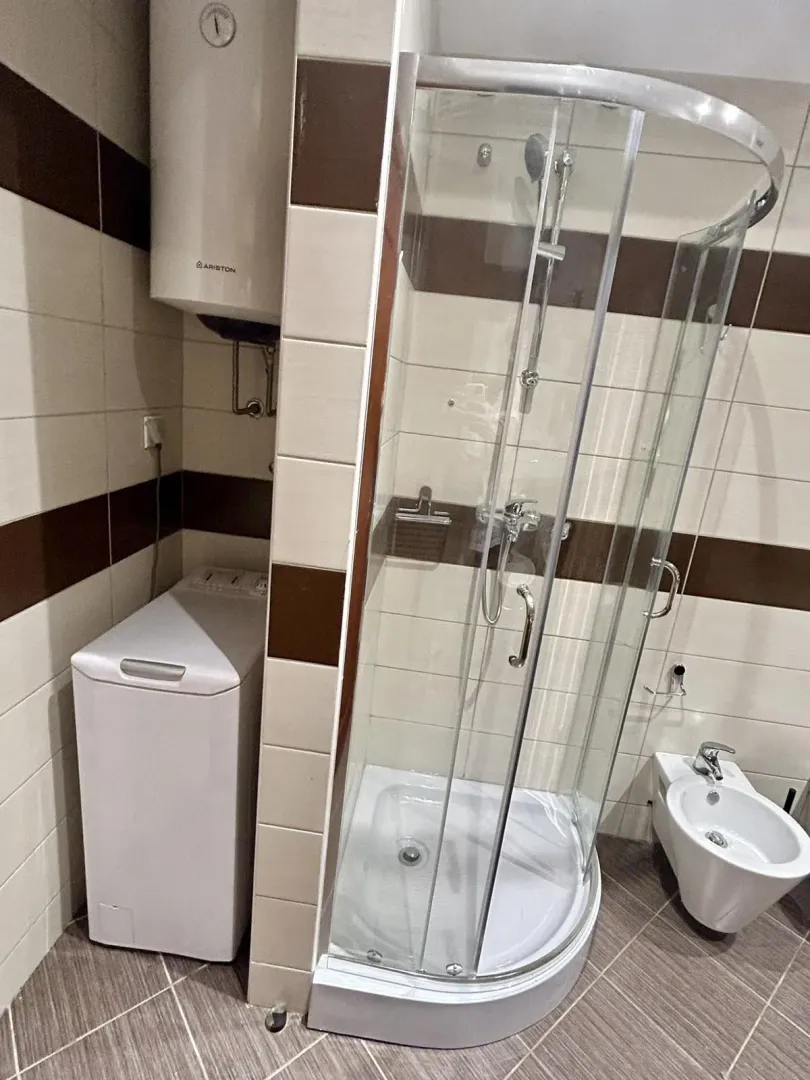 A bathroom featuring a shower cabin, bidet, and washing machine.