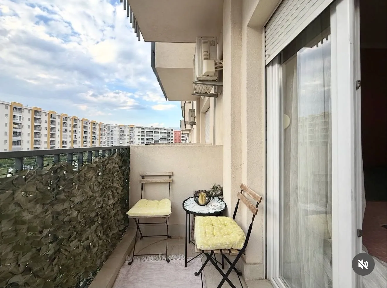 Manji namješten balkon sa stolom i dvije stolice i pogledom na zgrade.