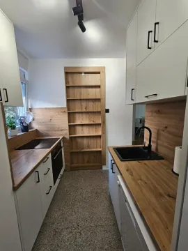 Moderna kuhinja sa bijelim elementima, drvenim radnim površinama i ugradnom policom. - image 10