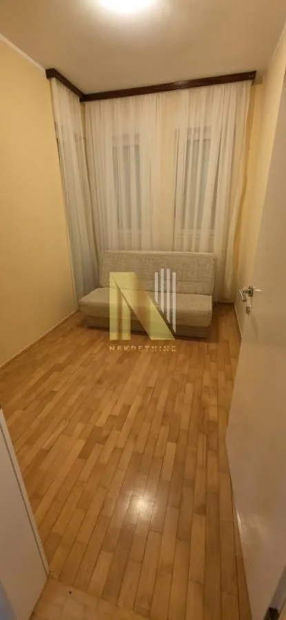 Manja soba sa kaučem i parketom na podu.