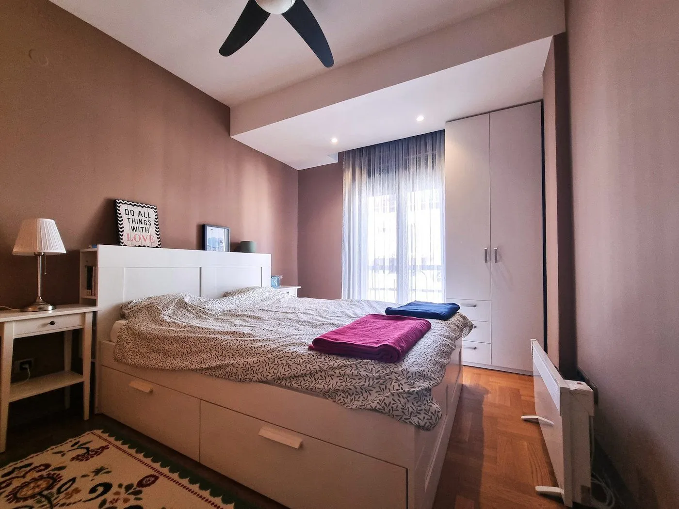 Namještena spavaća soba sa bračnim krevetom, plakarom i prozorom.