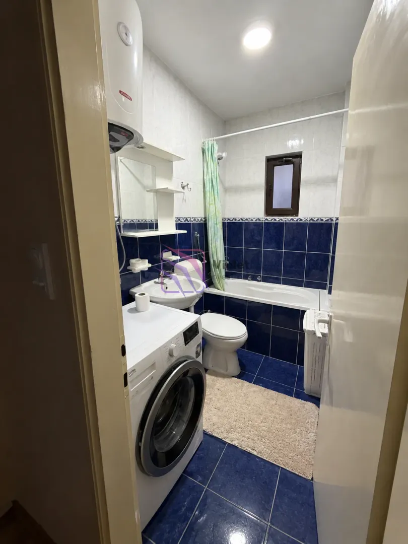 Bathroom with blue tiles, bathtub, washbasin, toilet, and washing machine.