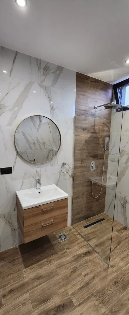Moderne kupatilo sa umivaonikom, ogledalom i tuš kabinom.
