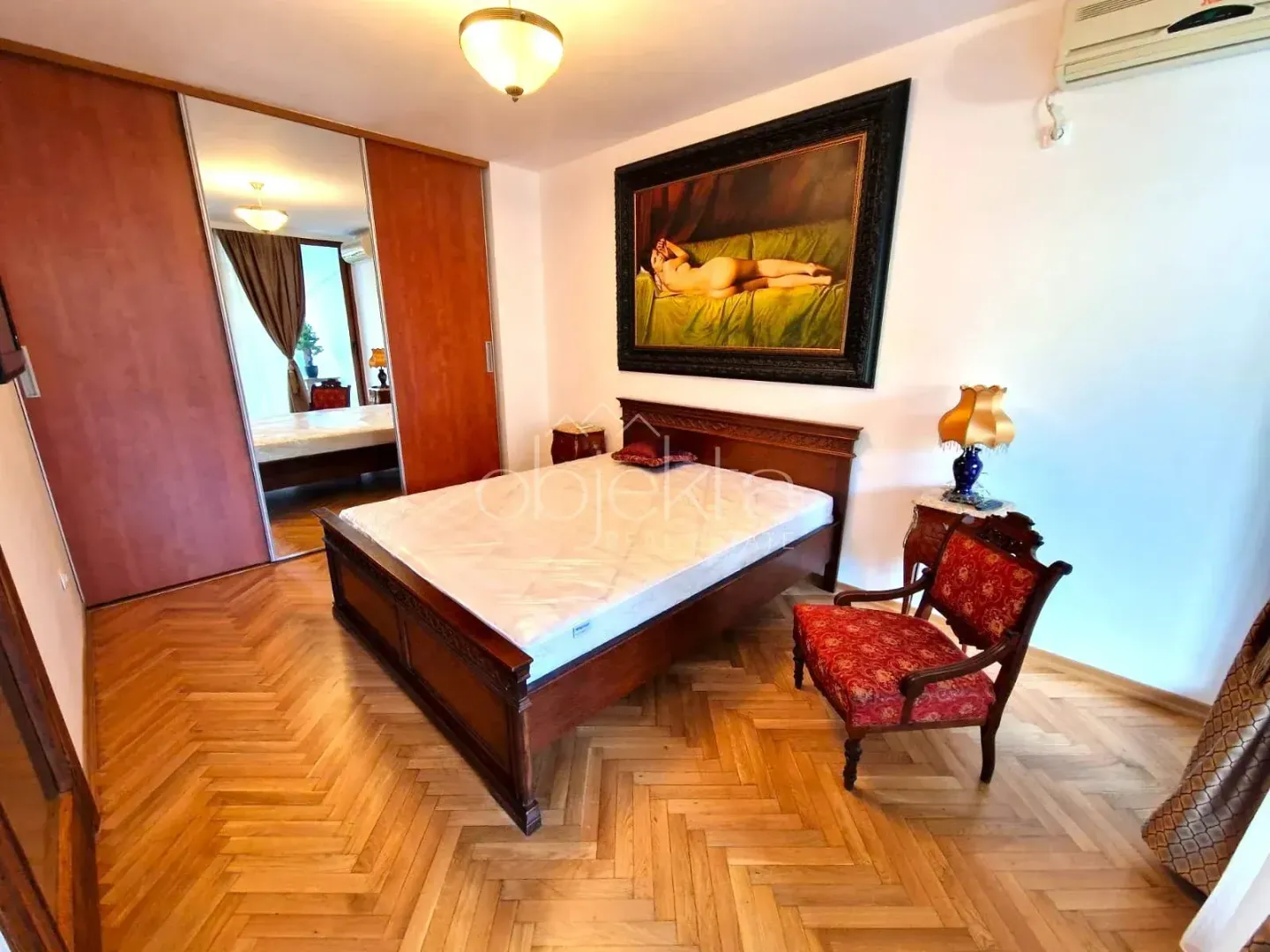 Bedroom with a double bed, wooden wardrobe with a mirror, and parquet flooring.