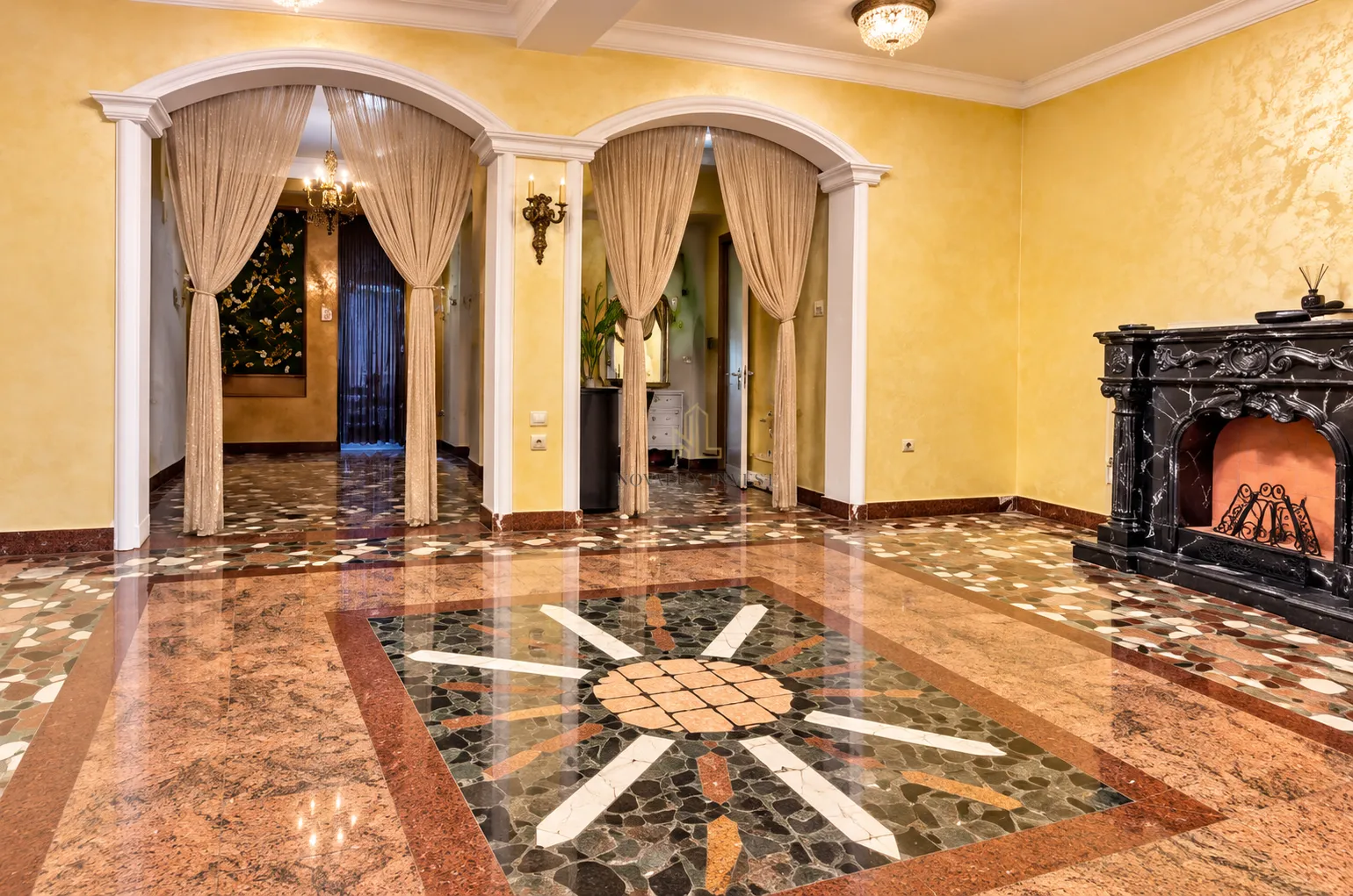 Spacious living room with a decorative fireplace, ornamental pillars, and a marble floor.