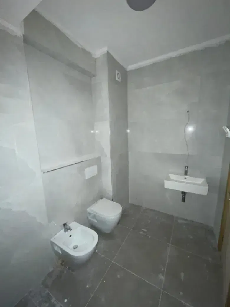 Manje kupatilo obloženo sivim pločicama sa sanitarijama.
