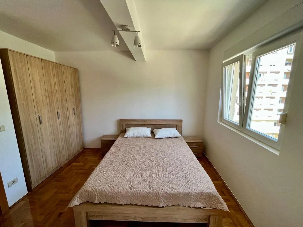 Furnished bedroom with a double bed, wardrobe, and parquet flooring.
