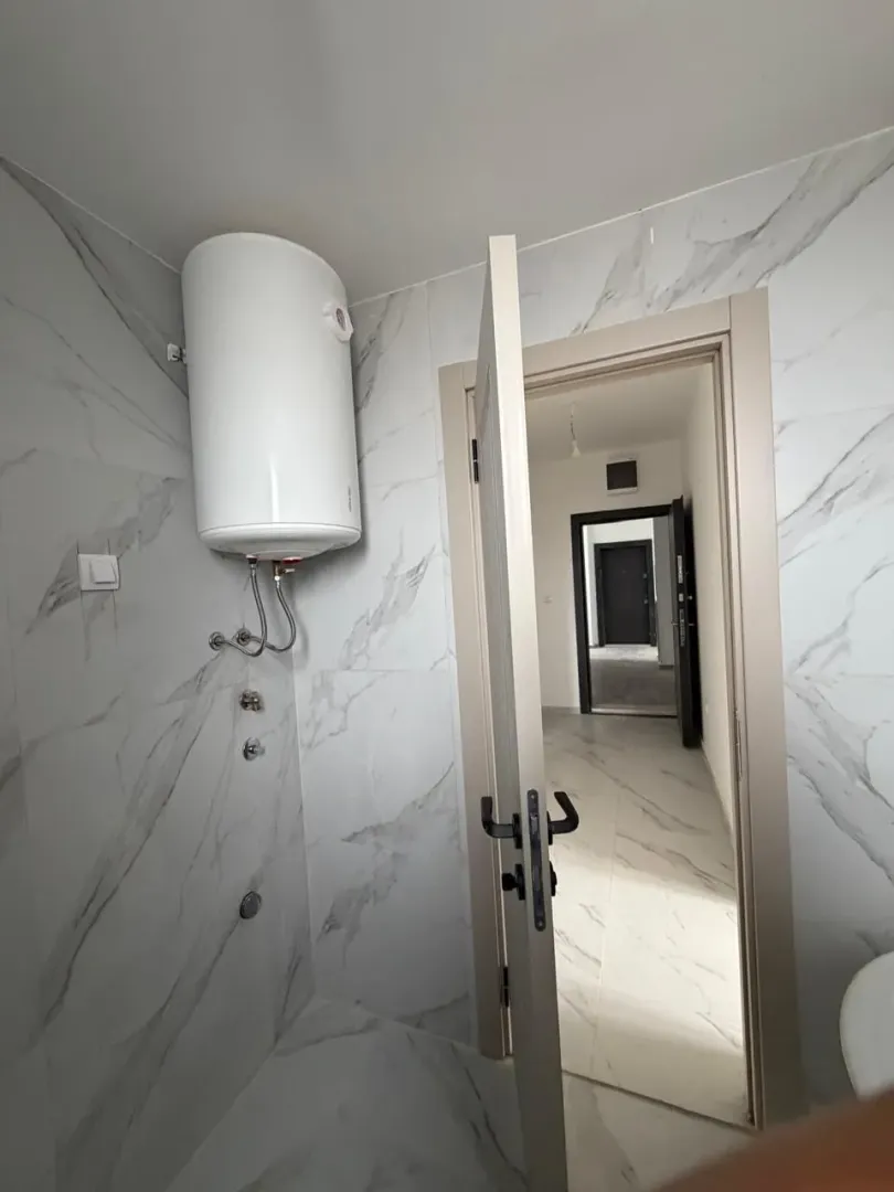 View of the bathroom with a water heater and an open door leading to the hallway.