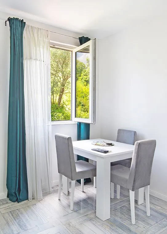 Dining table with chairs by the window overlooking greenery.