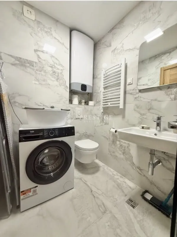 Modern bathroom lined with marble tiles featuring a washing machine.