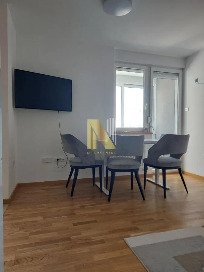 Dnevna soba sa trpezarijskim stolom, stolicama i televizorom na zidu.