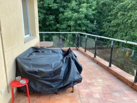 Spacious balcony with a glass railing and furniture covered with a protective cover. - image 3