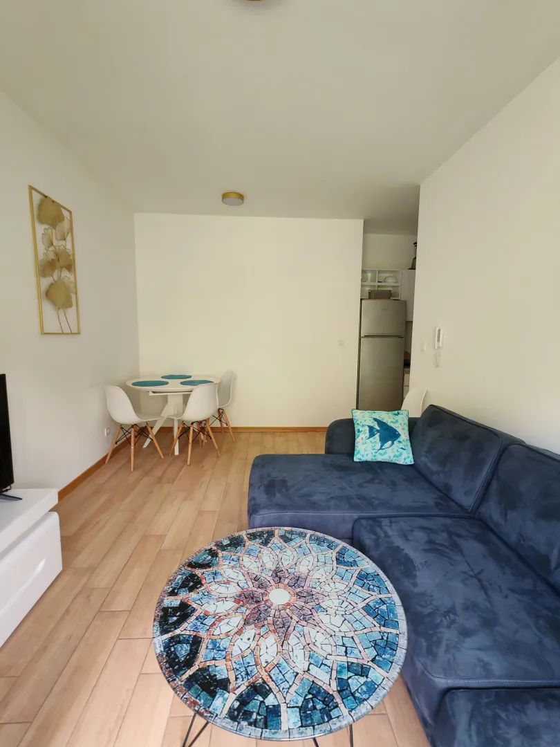 Living room with a sofa, coffee table, and a dining area in the background.