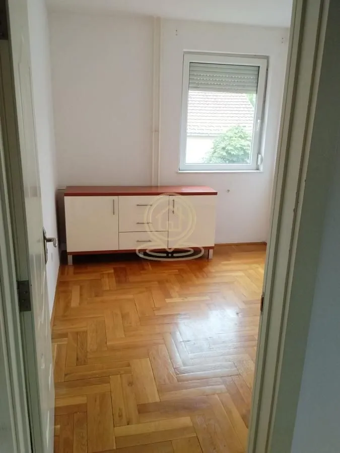Prazna soba sa parketom i komodom.