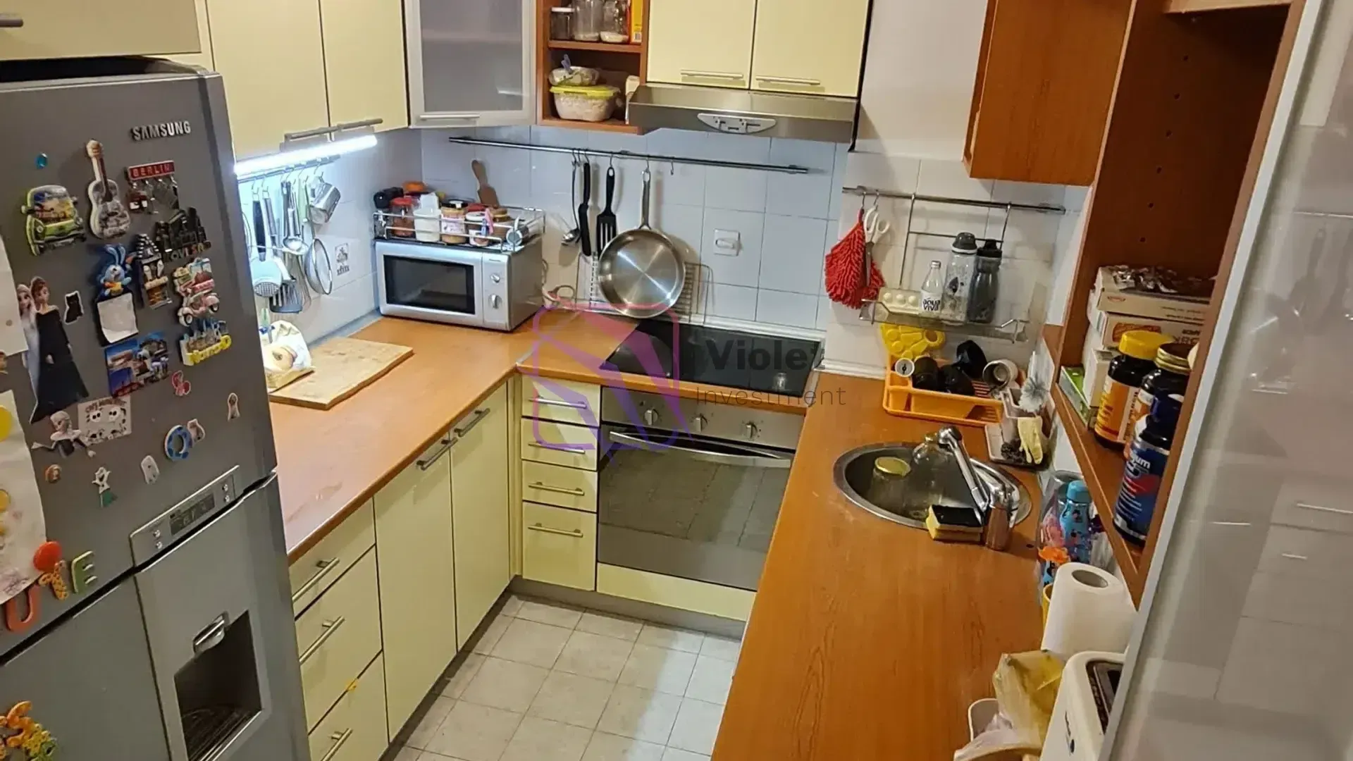 Manja opremljena kuhinja sa drvenim radnim površinama i belom tehnikom.