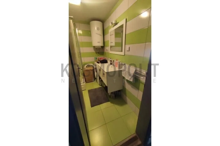 Kupatilo obloženo zelenim i belim pločicama sa umivaonikom i bojlerom.