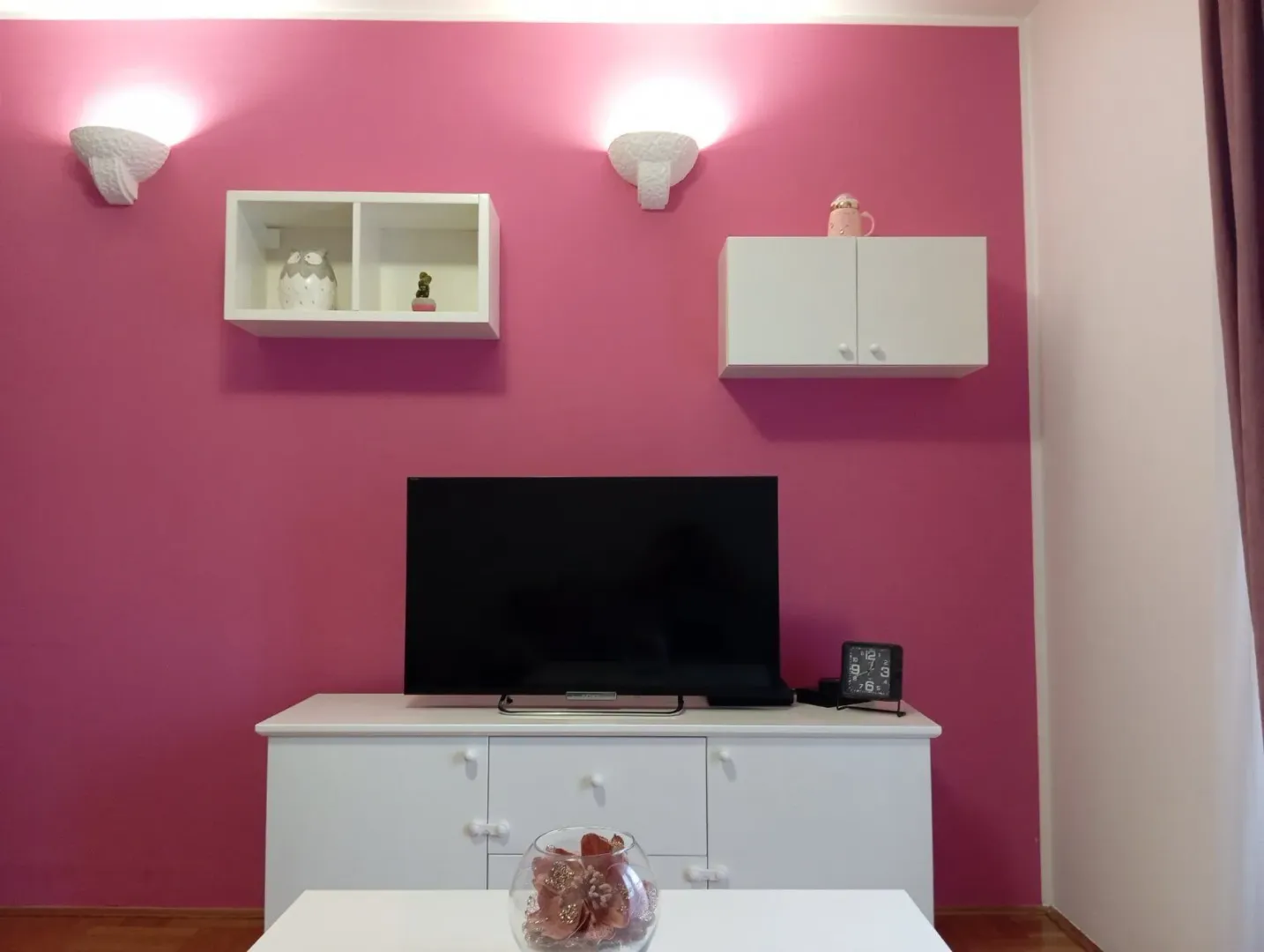 Dnevna soba sa ružičastim zidom i TV-om.
