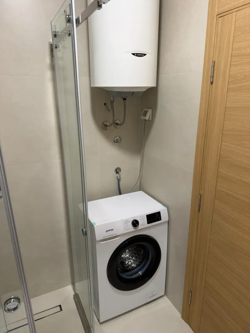 Bathroom with a shower cabin, water heater, and washing machine.