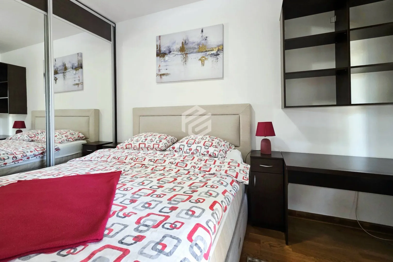 Furnished bedroom with a double bed, mirrored wardrobe, and a desk.