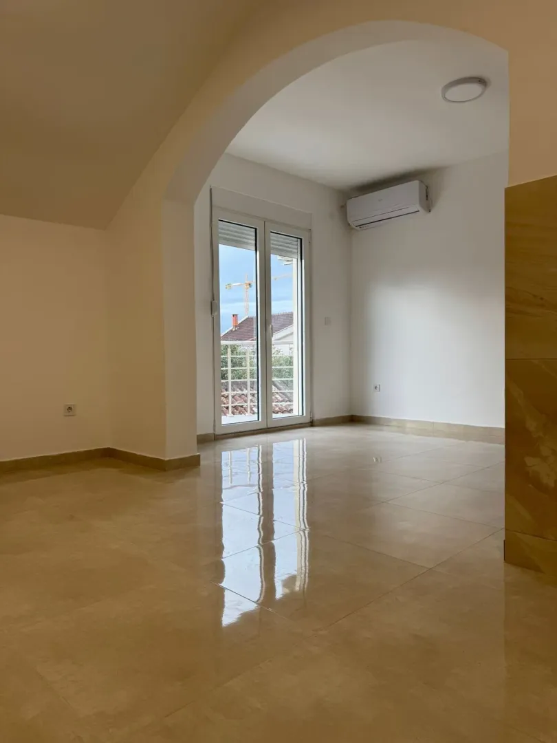An empty, bright room with tiled flooring and access to a balcony.