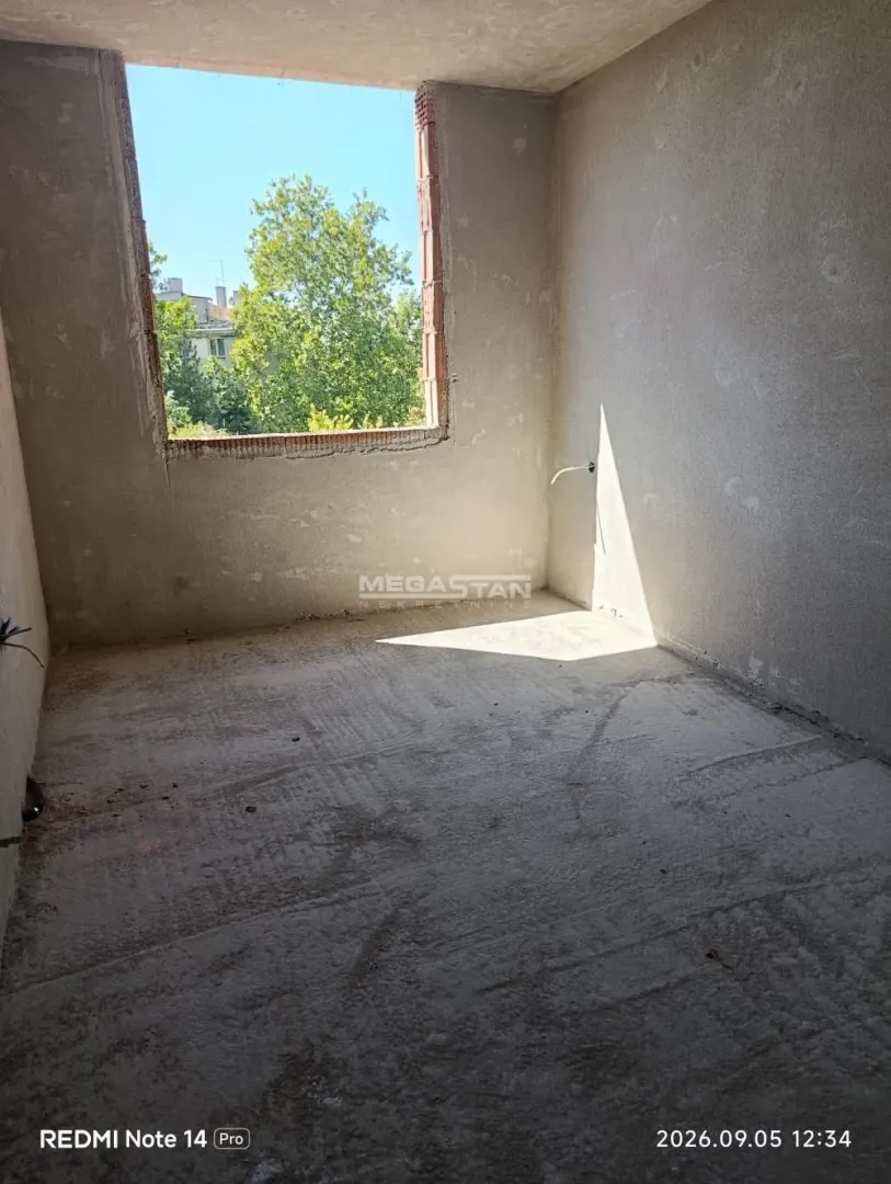 Unfinished room in grey phase with a window and a view of greenery.