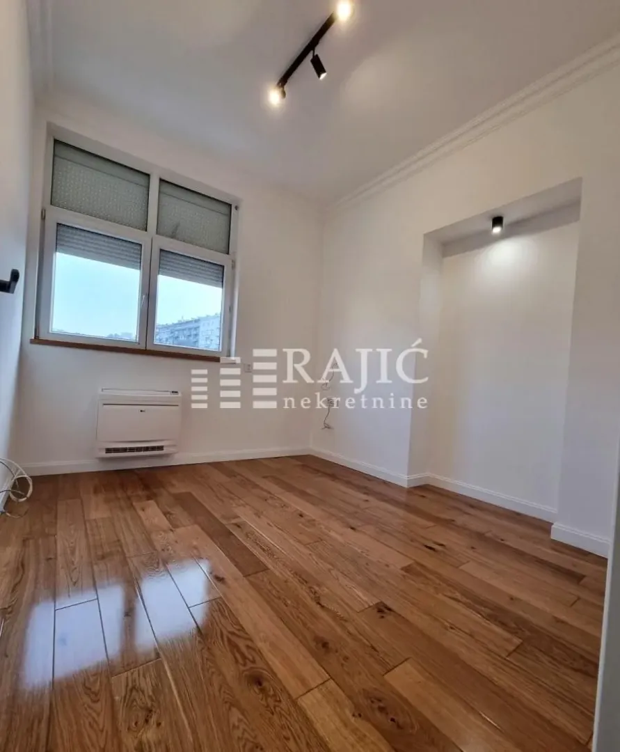 Empty room with wooden flooring, white walls, and a window.
