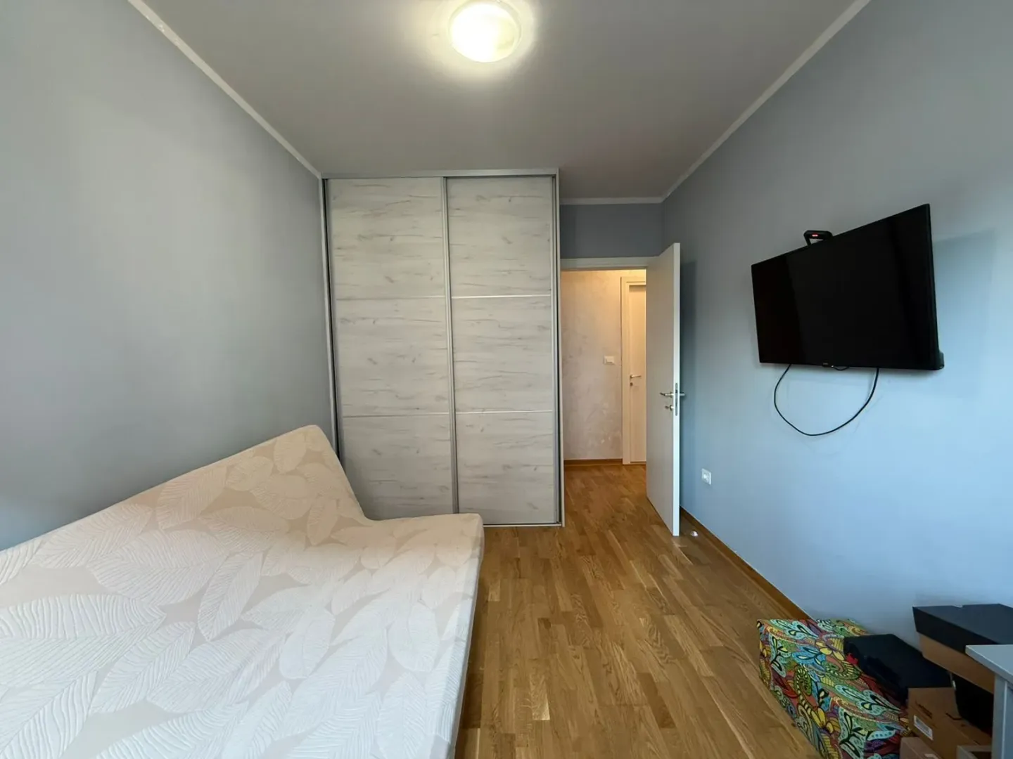 Manja spavaća soba sa krevetom, garderoberom i zidnim televizorom.